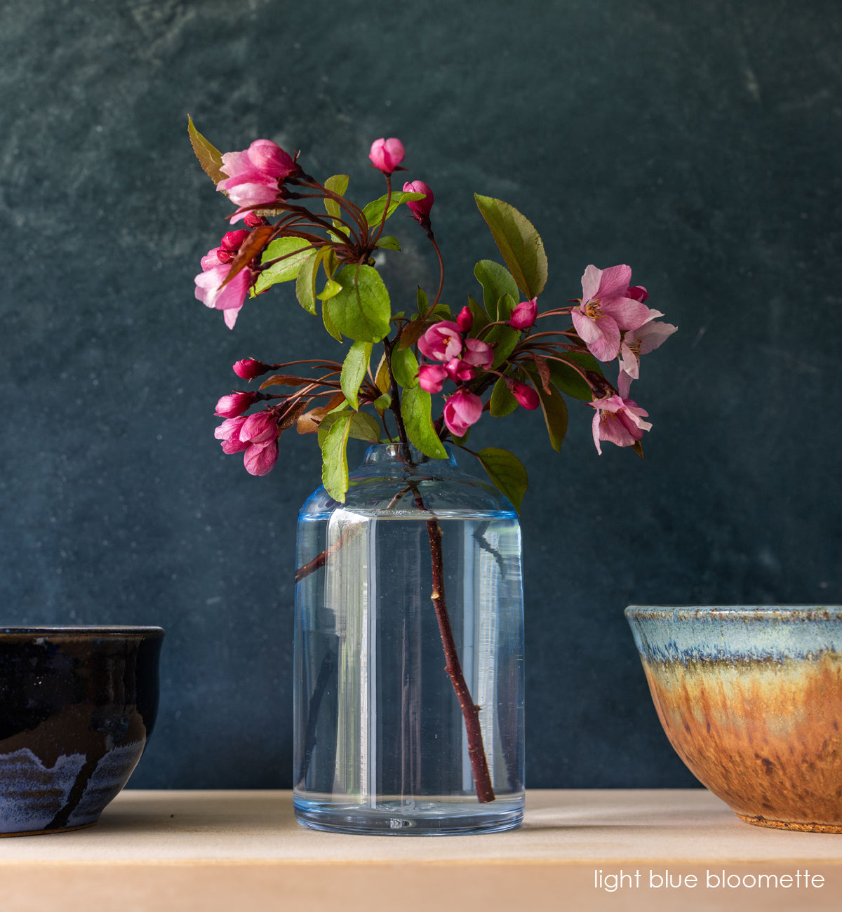 light blue bloomette on butcher block table in between tow bowls. blue background