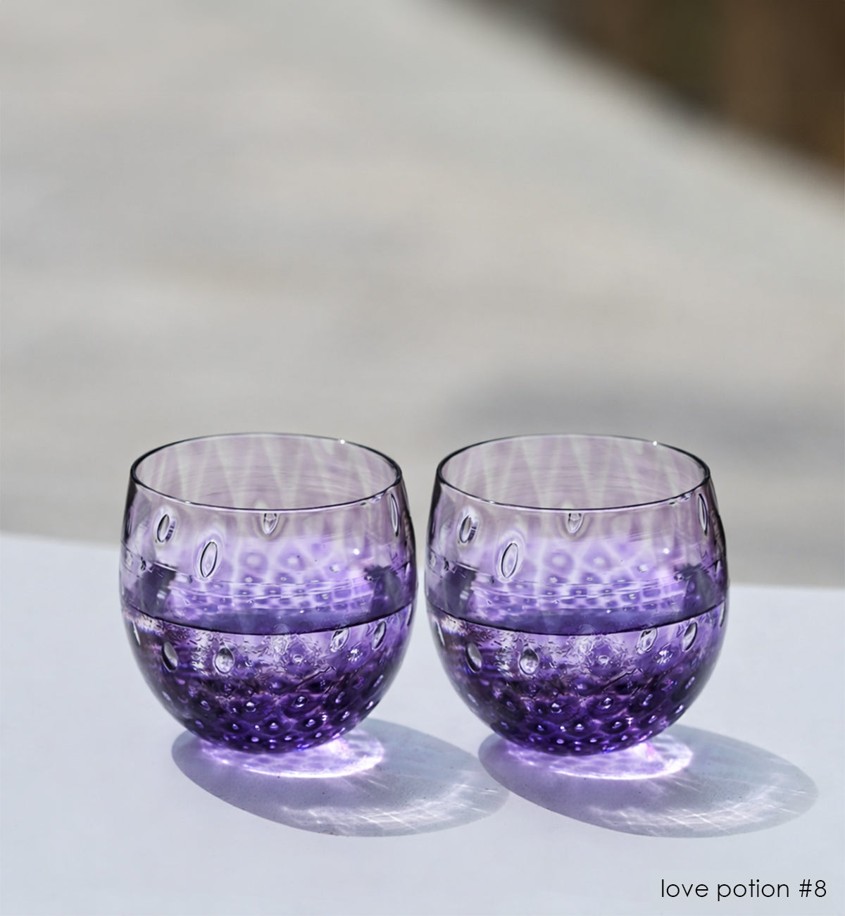 two love potion #8, a deep purple hand-blown drinking glass with a bubble pattern, sitting on white surface in sunlight.