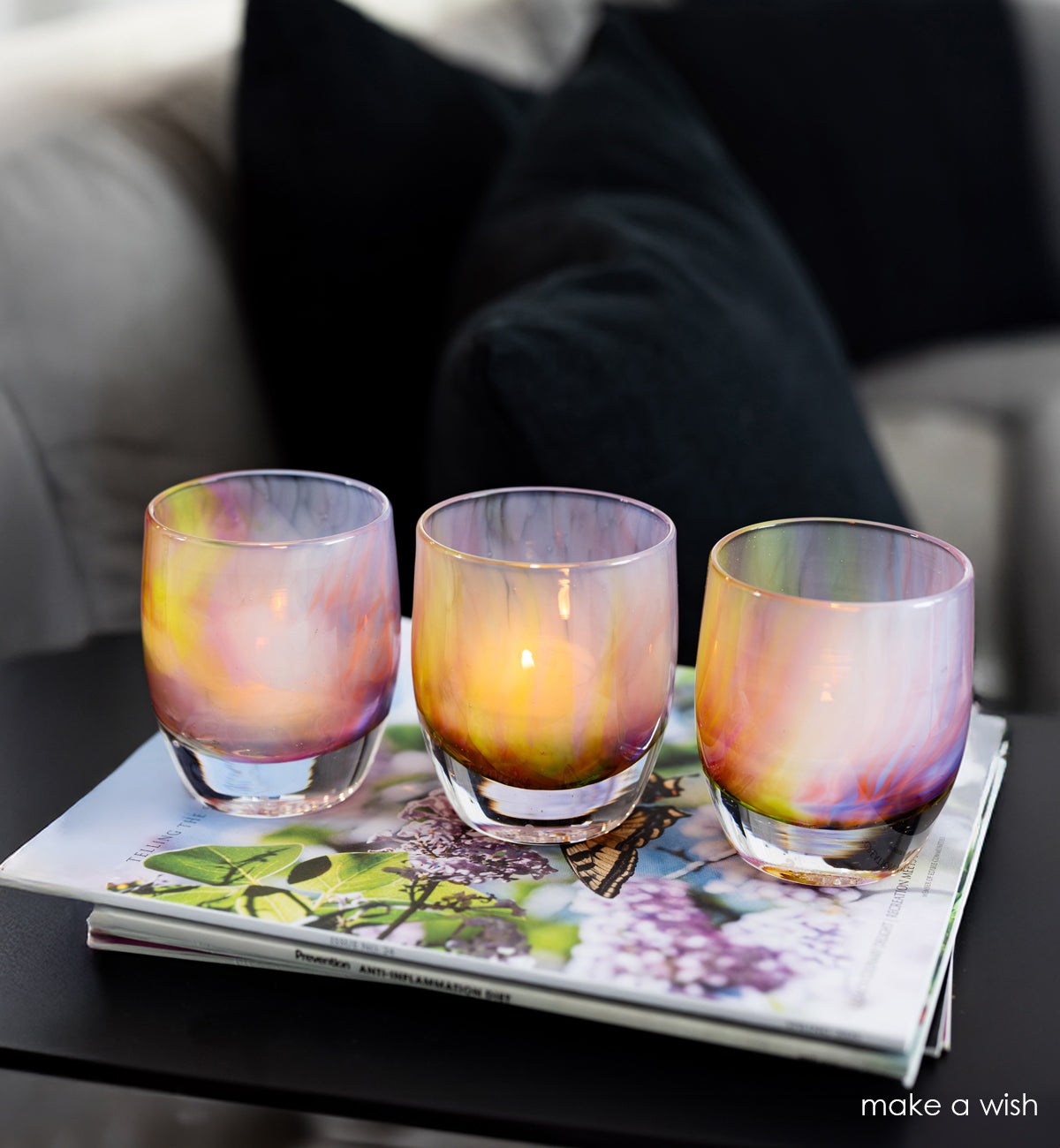 Three colorful glass votives on a magazine with a blurred background