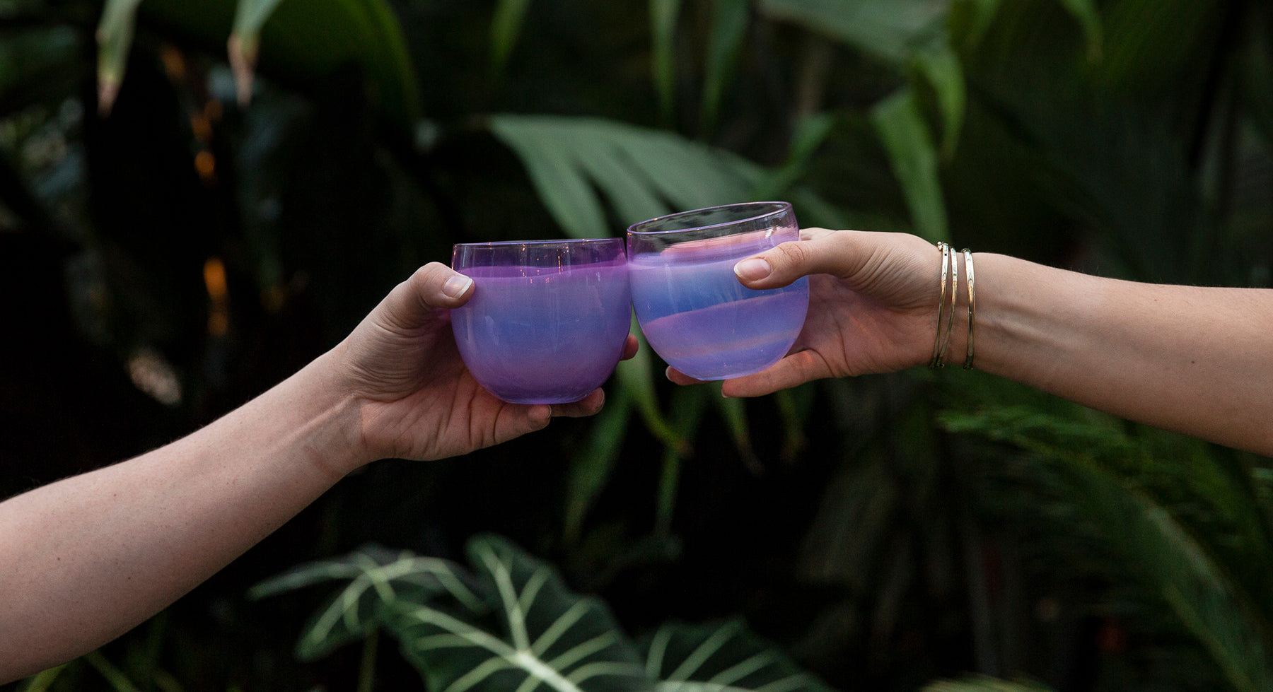 2 mama drinkers being cheersed outside. hand-blown glass drinking glasses in a beautiful purple hue.