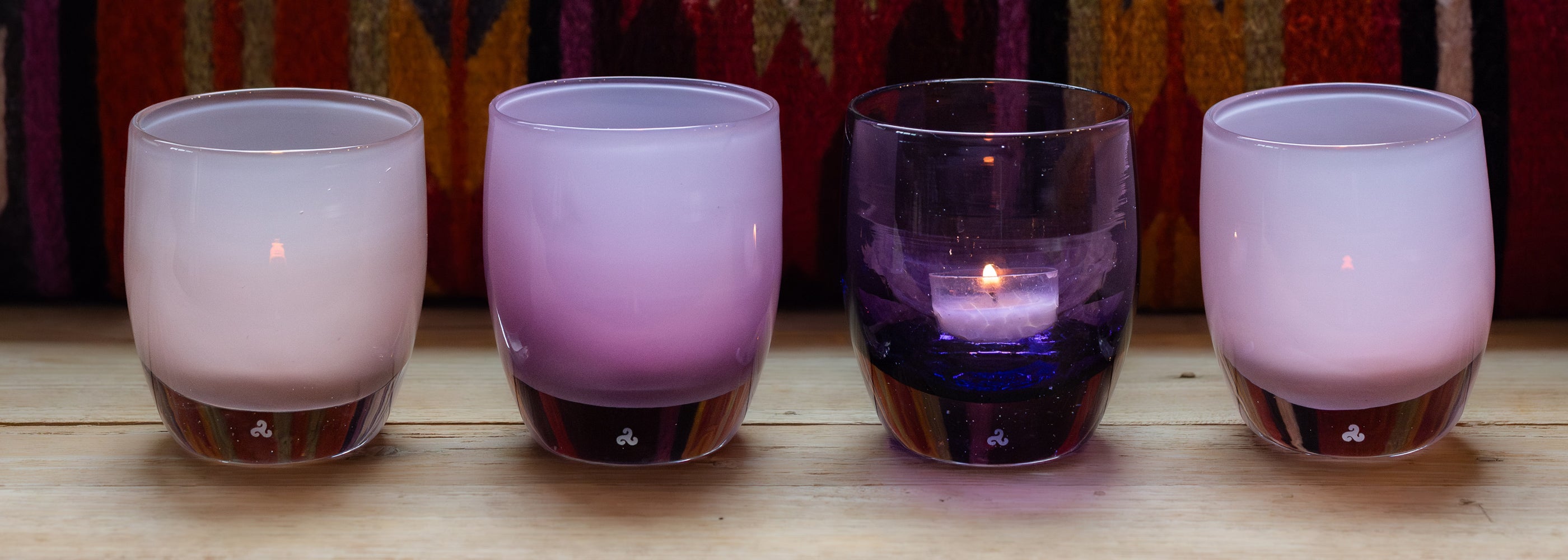 shades of purple glassybaby hand-blown glass candle holders on wood bench.