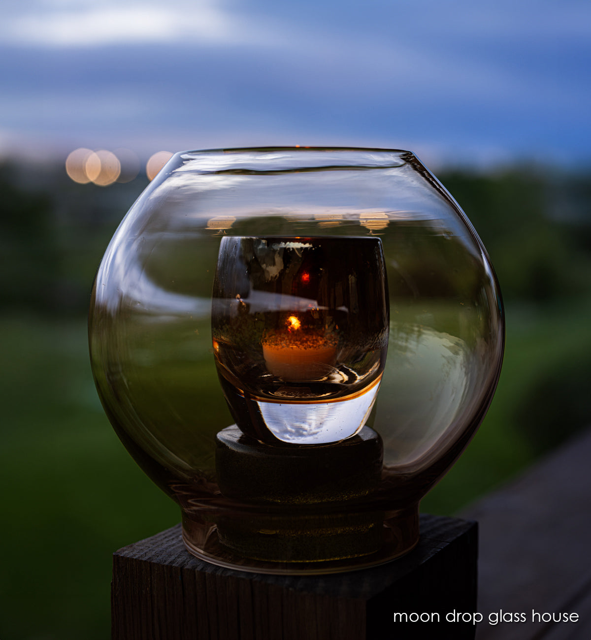 moon drop round glass house, hand-blown glass hurricane with glassybaby in it one wood post at dusk.