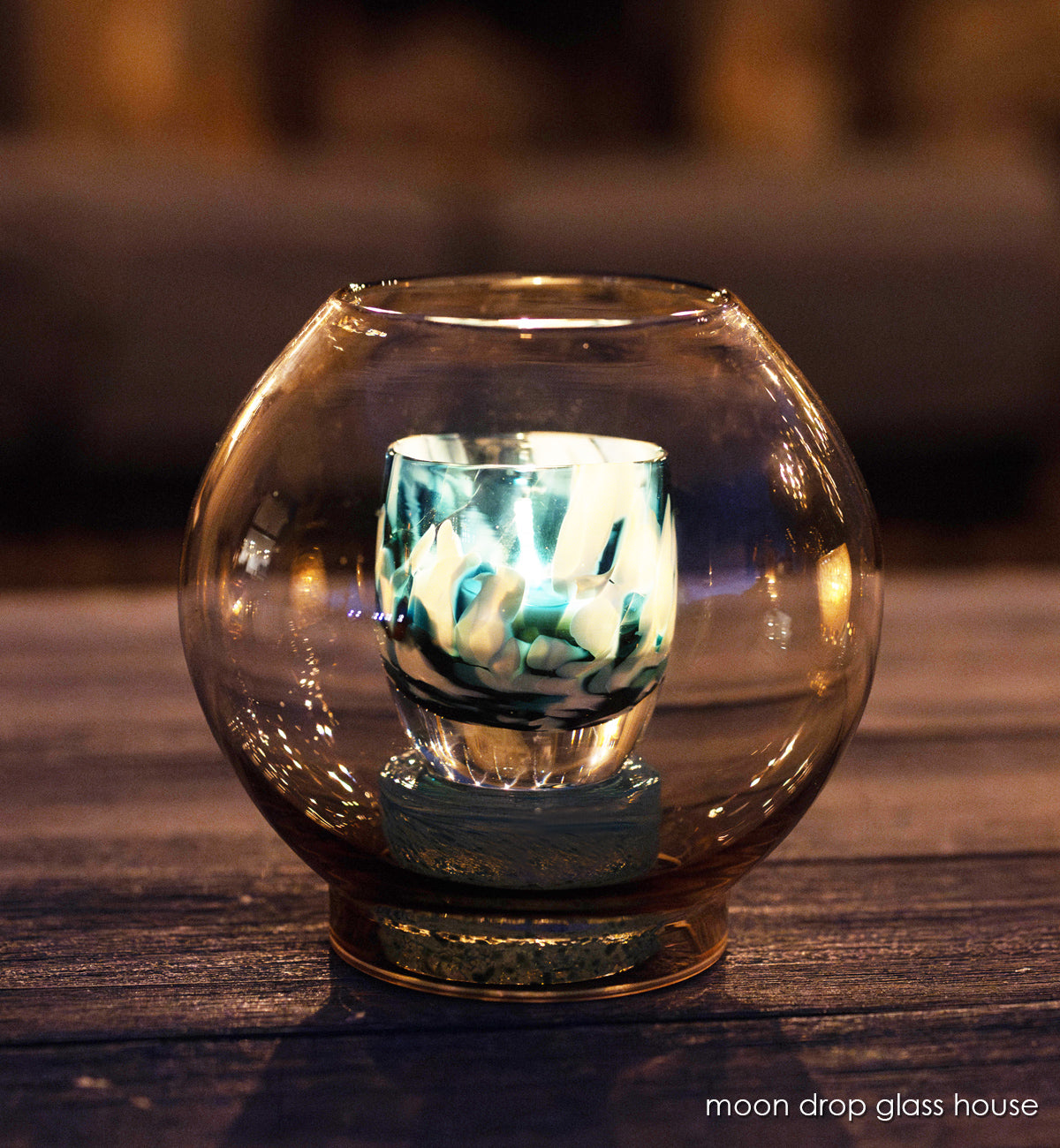 moon drop round glass house, hand-blown glass hurricane with glassybaby in it one wood table at night.