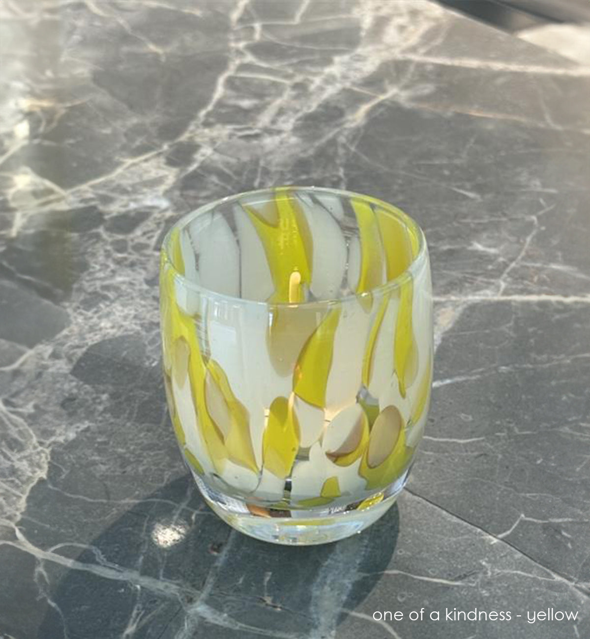 hand-blown glass candle holder with yellow and white patterns on a marble surface