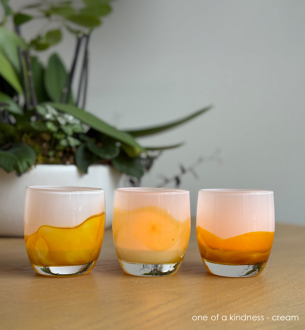 Three yellow and cream coloration glass candle holders on a wooden surface with a plant in the background.