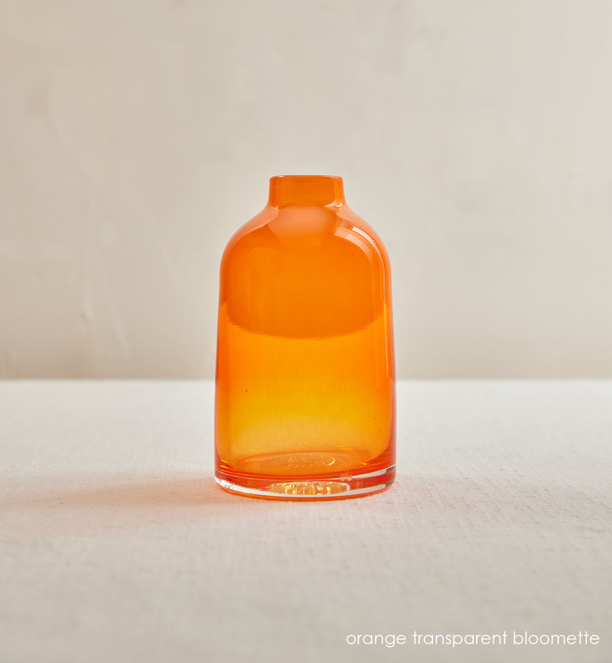 orange transparent bloomette, transparent orange hand-blown glass flower bud vase in front of a cream background.