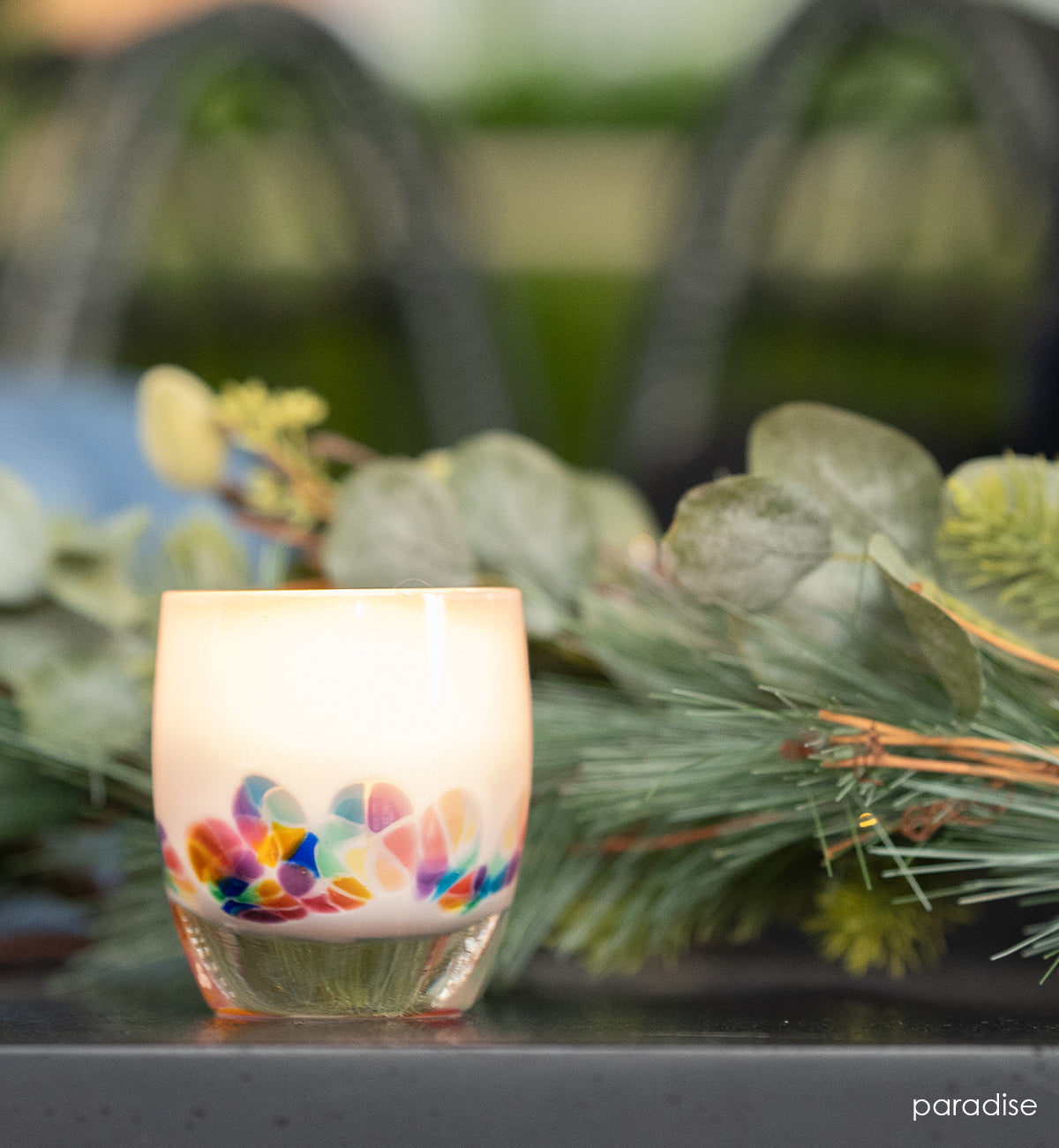 paradise white rainbow flowers hand-blown glass votive candle holder on an outdoor counter surrounded by greenery.