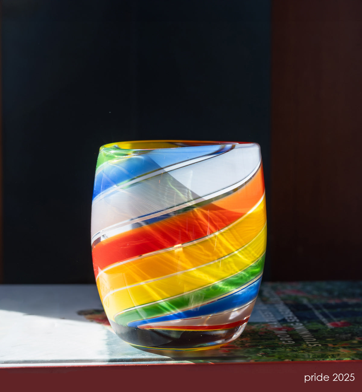 'pride 2025' glassybaby with rainbow swirls, hand-blown glass candle holder sitting on a book