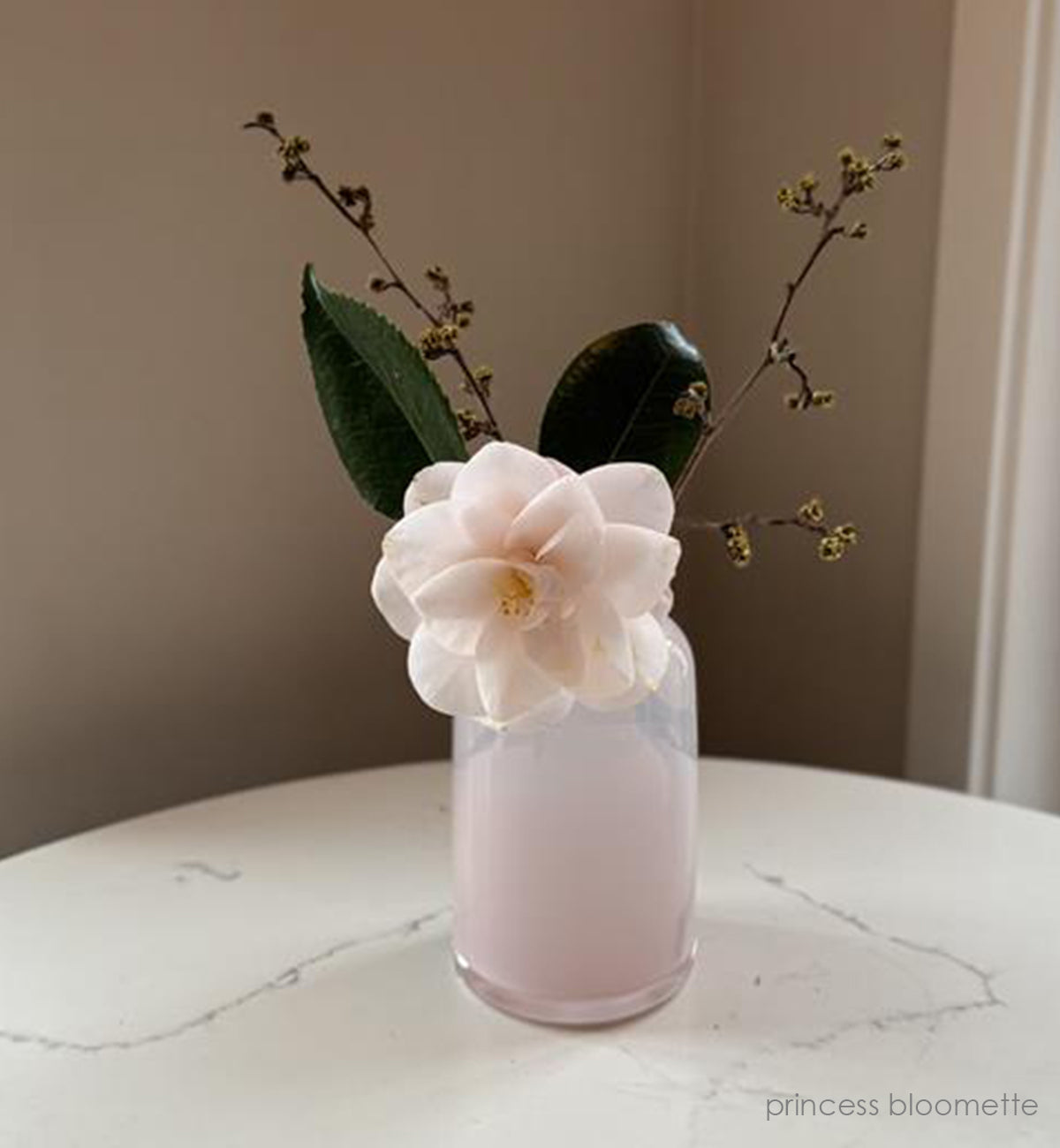 'priness bloomette' light pink opaque hand-blown glass flower bud vase holding pink flower on white and grey marble table.