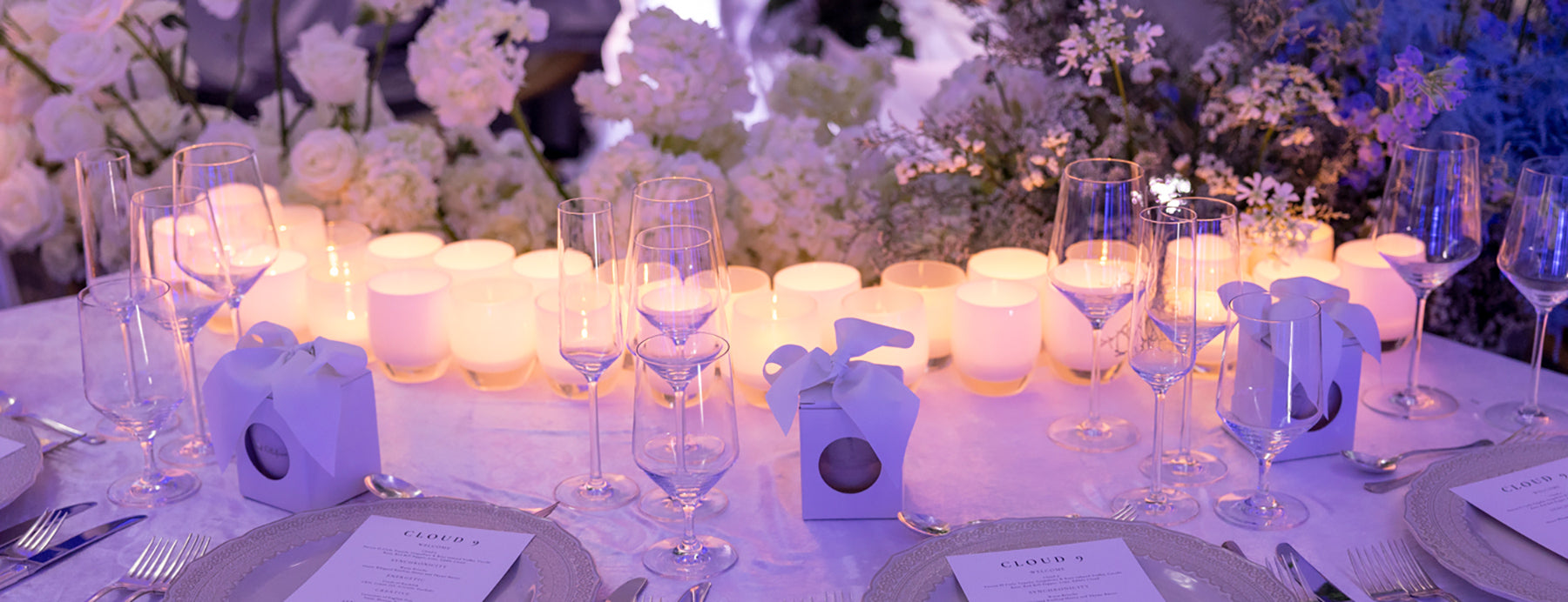 glowing white hand-blown glass candle holders part of a beautiful table scape with flowers, menus and wine glasses.