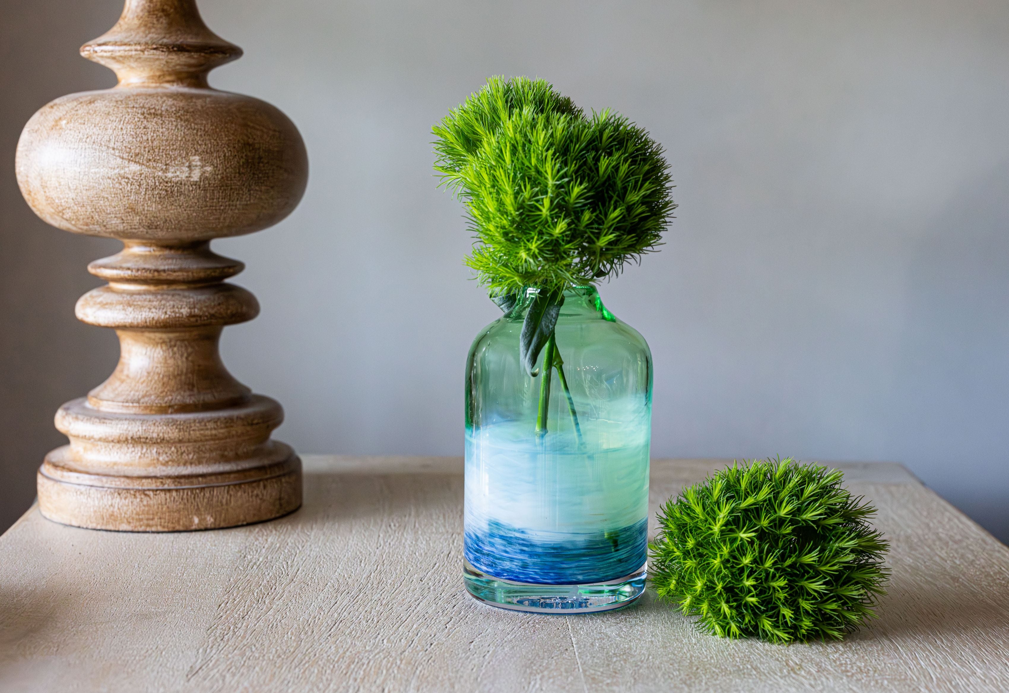 glassybaby bloomette transparent glass vase with blue and white accents on a side table with a lamp and flowers inside the vase