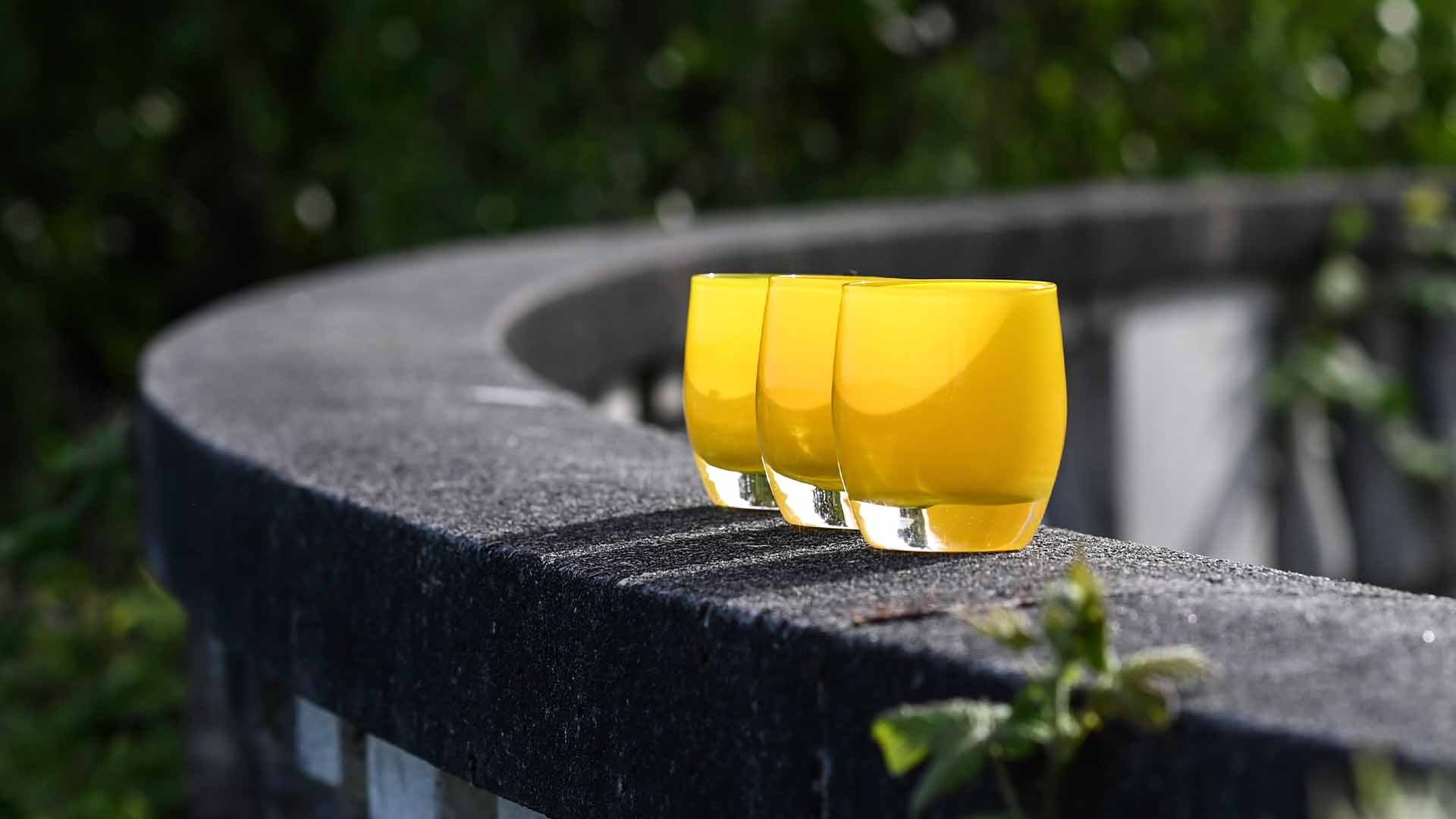 sunshine yellow basking on a stone wall in a garden. Hand-blown glass votive candle holder.