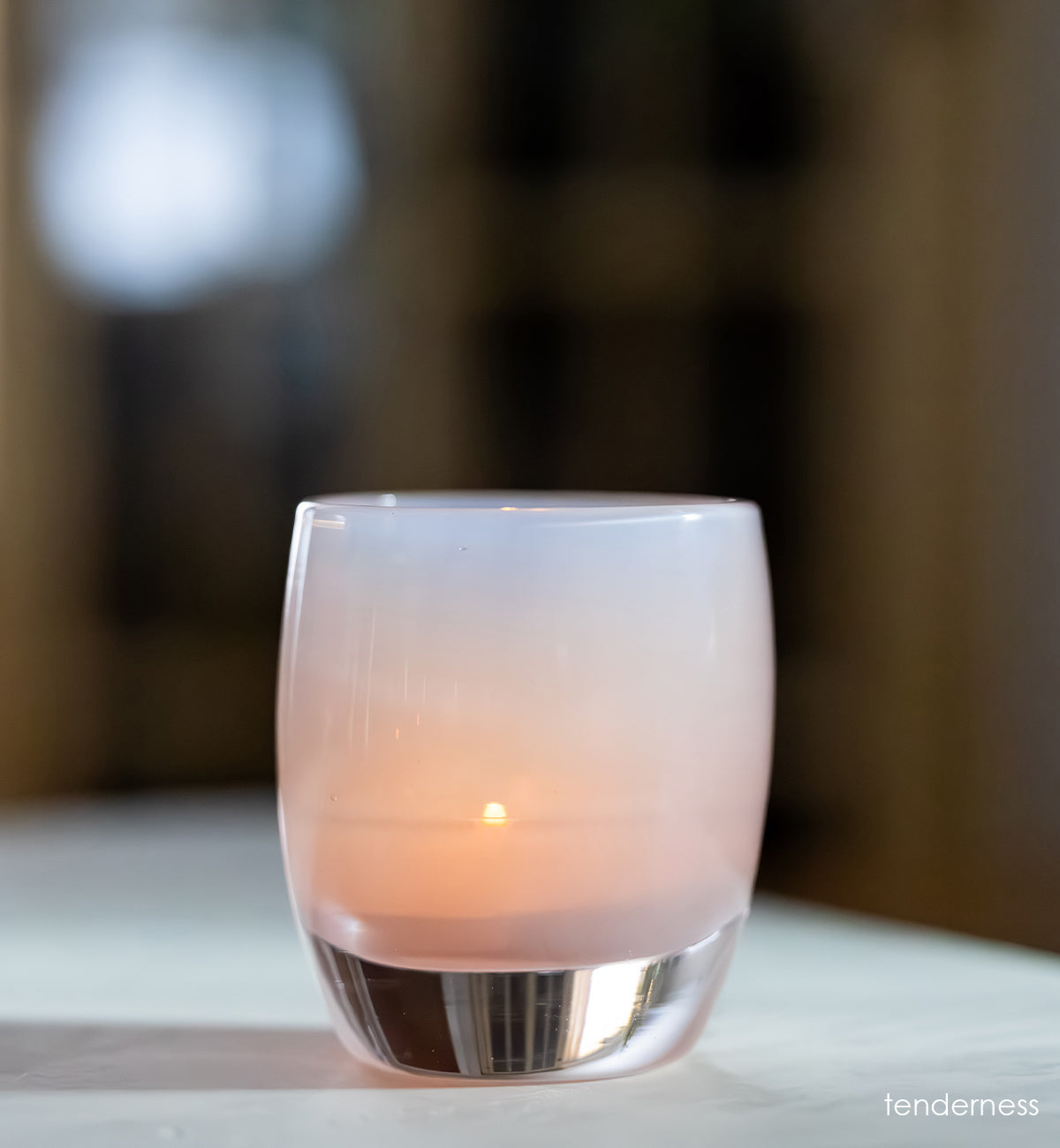 tenderness, a soft-purple/pink hand-blown glass votive candle holder on a table.