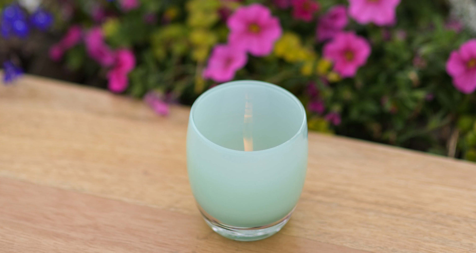 thank you, light green hand-blown glass candle holder sitting on a wood table with flowers in the background.