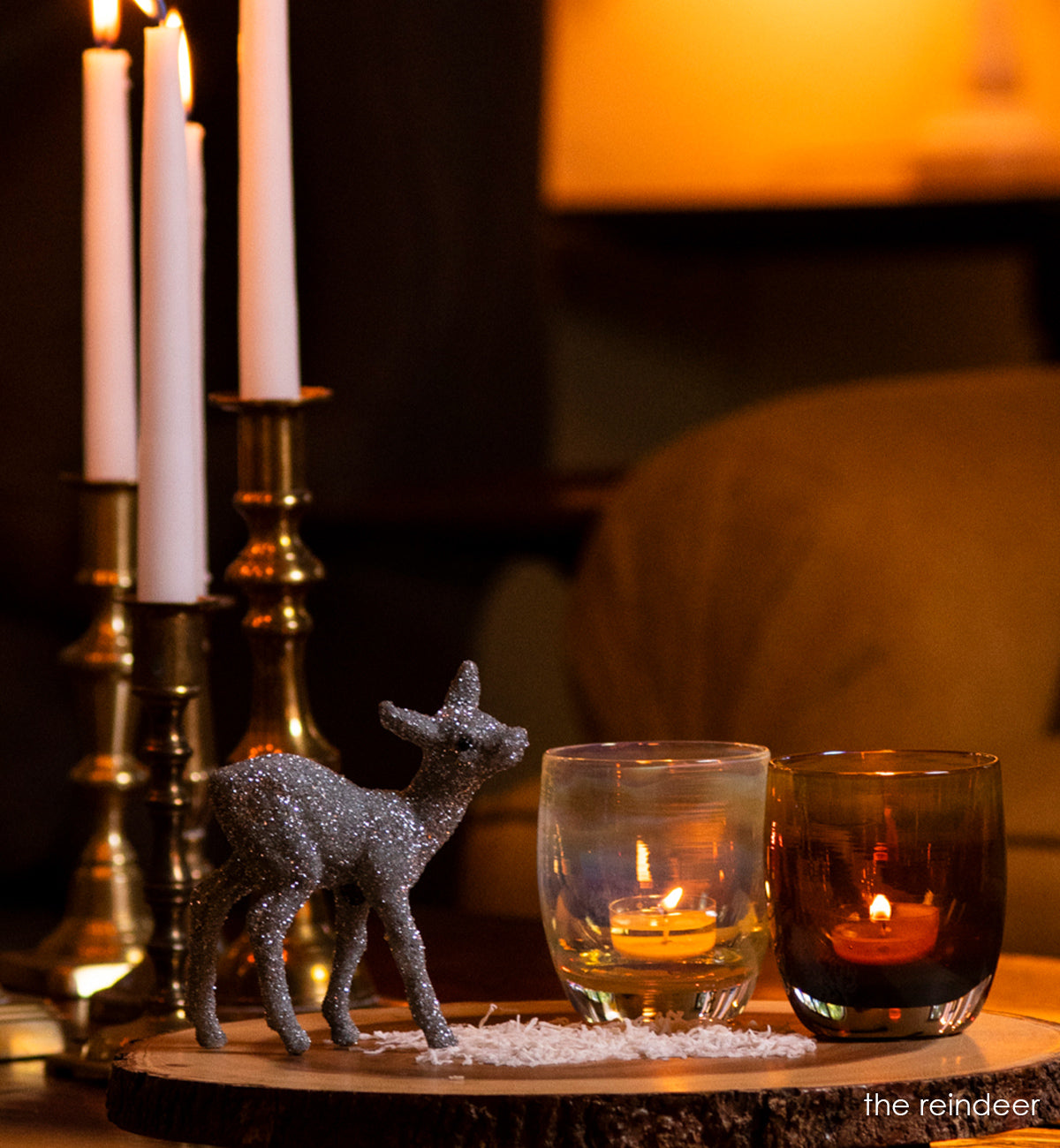 a set of iridescent brown and yellow translucent glassybaby candle holders. 'the reindeer', 'blitzen' and 'vixen', sit on a wood table next to a reindeer figurine and 4 tall candle sticks.