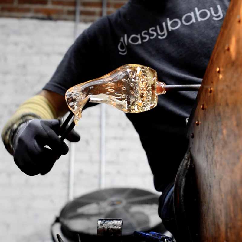 glassblower trimming 'yes' glassybaby in the hot shop.