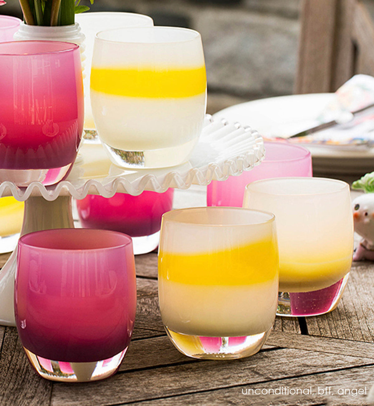 unconditional, white with yellow stripe, hand-blown glass votive candle holder. Paired with bff and angel on an outdoor wood table with flowers and a cake tray.