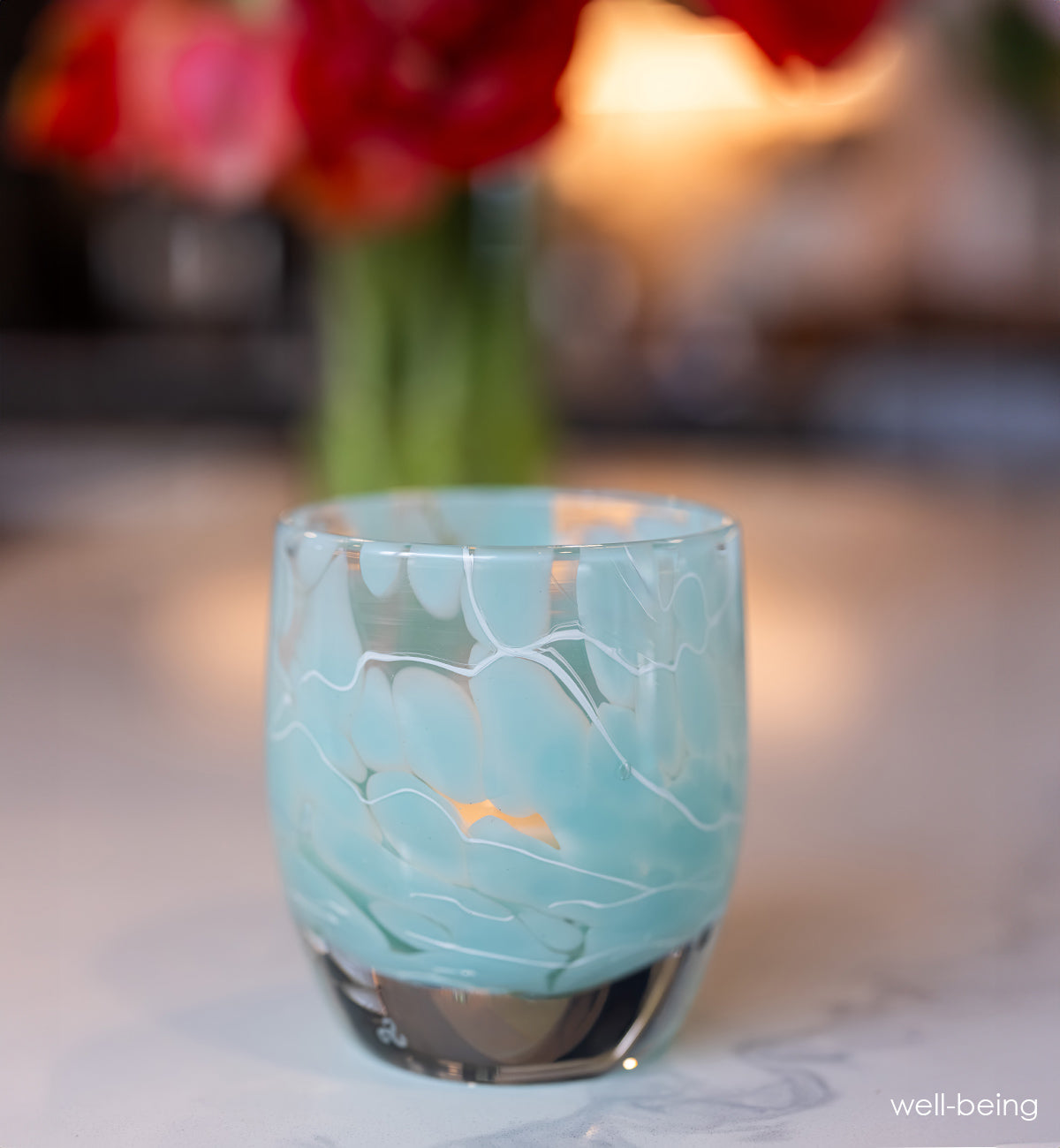 Turquoise with white marbled pattern glass candle holder with a blurred floral background