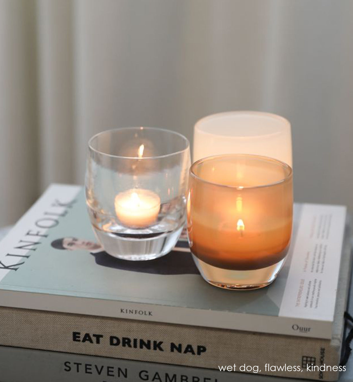 wet dog, two toned brown, hand-blown glass votive candle holder on a stack of coffee table books with flawless and kindness.