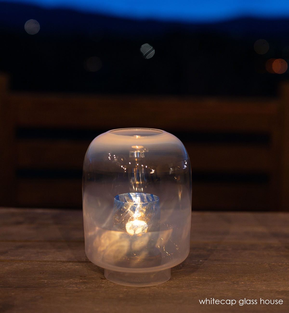 whitecap glass house, hand-blown glass hurricane with 'open window' in it one wood table at night.