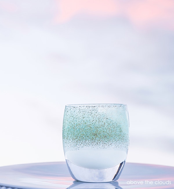 above the clouds, teal and silver, hand-blown glass votive candle holder on a light outdoor surface.