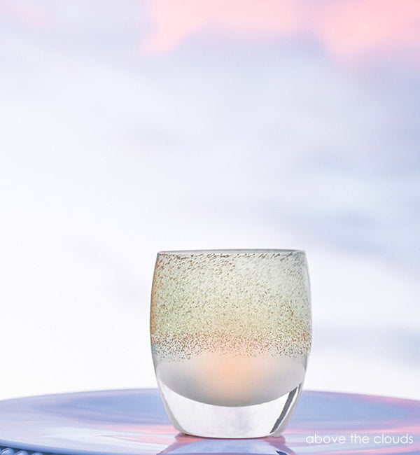 above the clouds, teal and silver, hand-blown glass votive candle holder lit on a light outdoor surface.