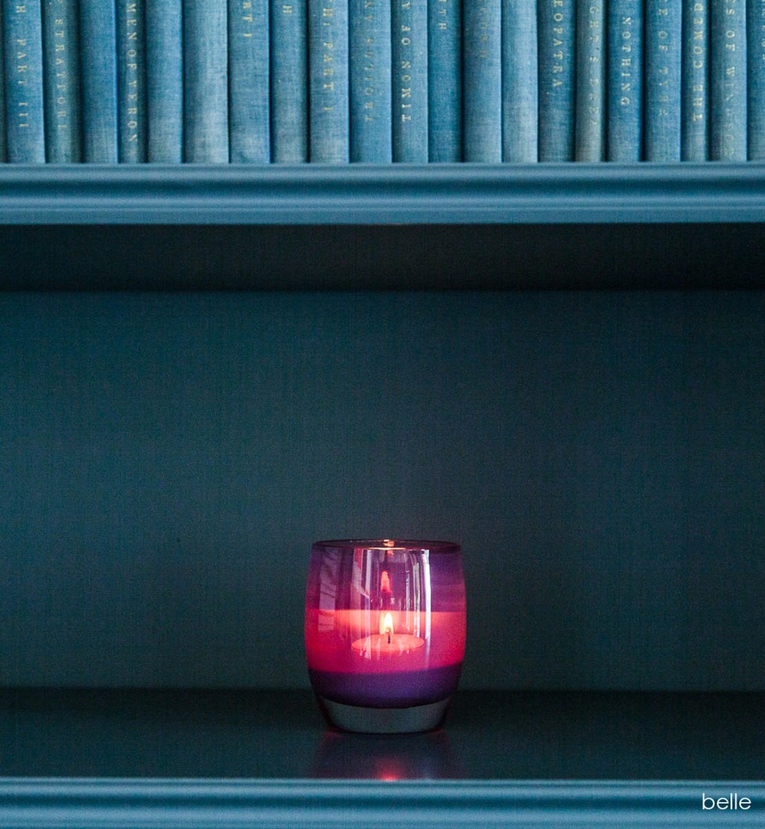 belle regal purple hand-blown glass votive candle holder, on a blue bookshelf.