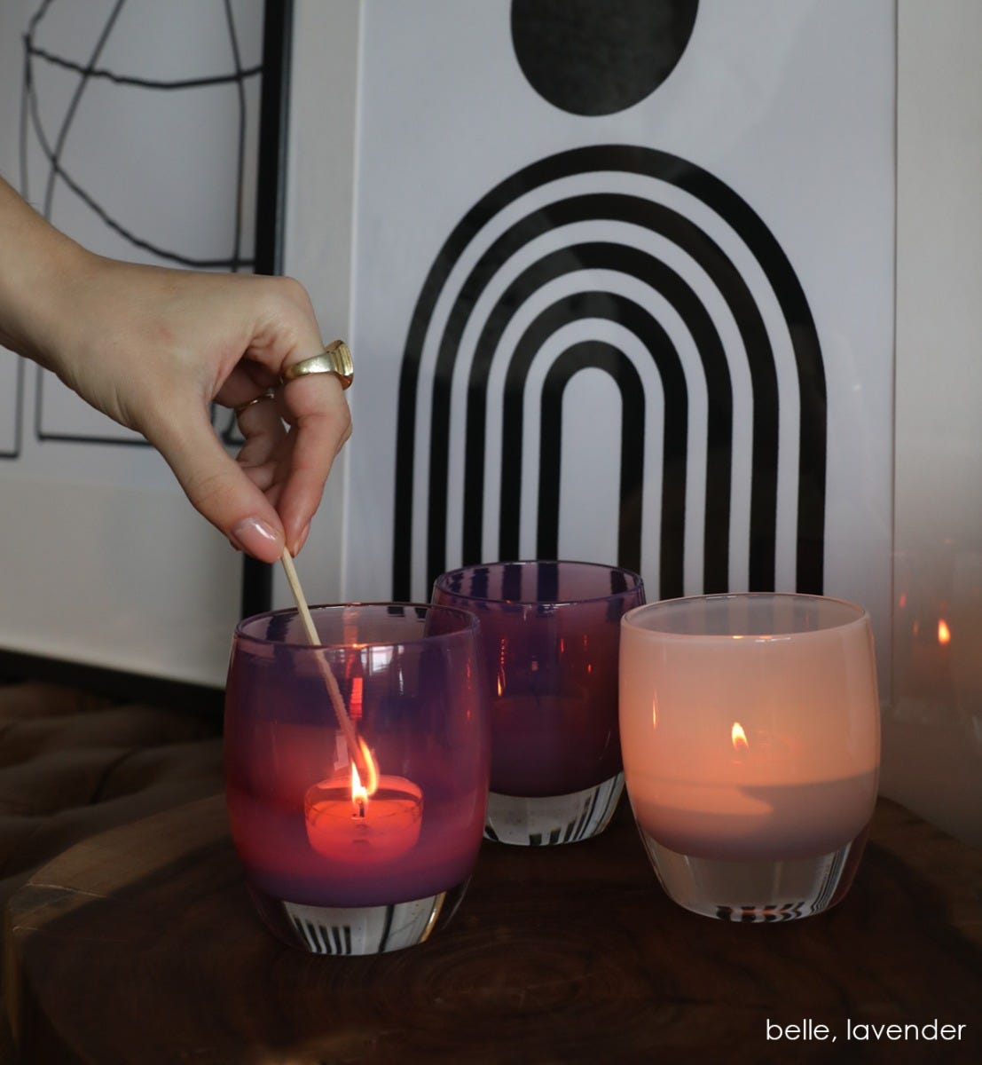 two belle regal purple hand-blown glass votive candle holders next to lavender in front of black and white framed art..