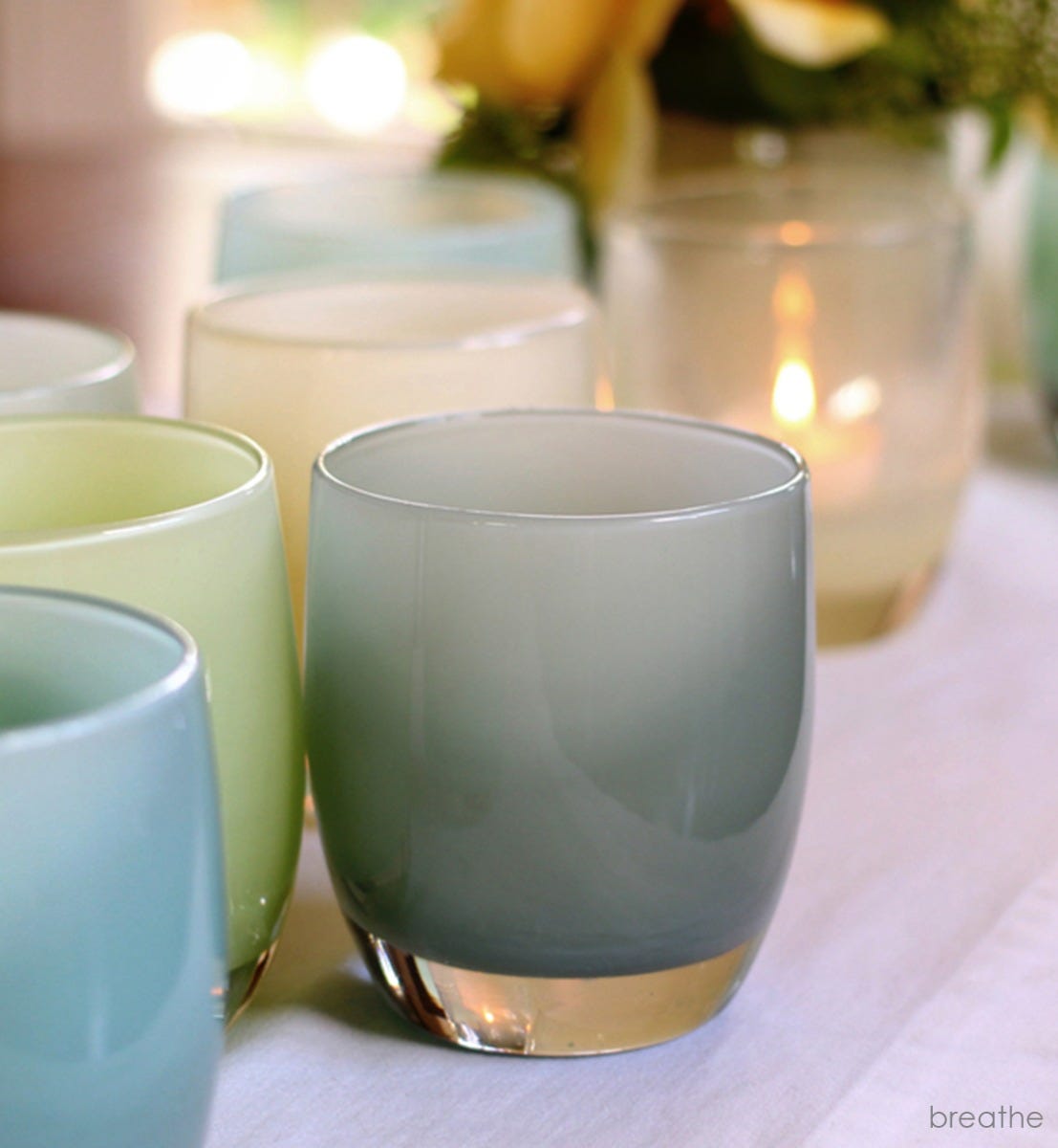 breathe sea green hand-blown glass votive candle holder on a white tablecloth with other earth toned glassybaby.