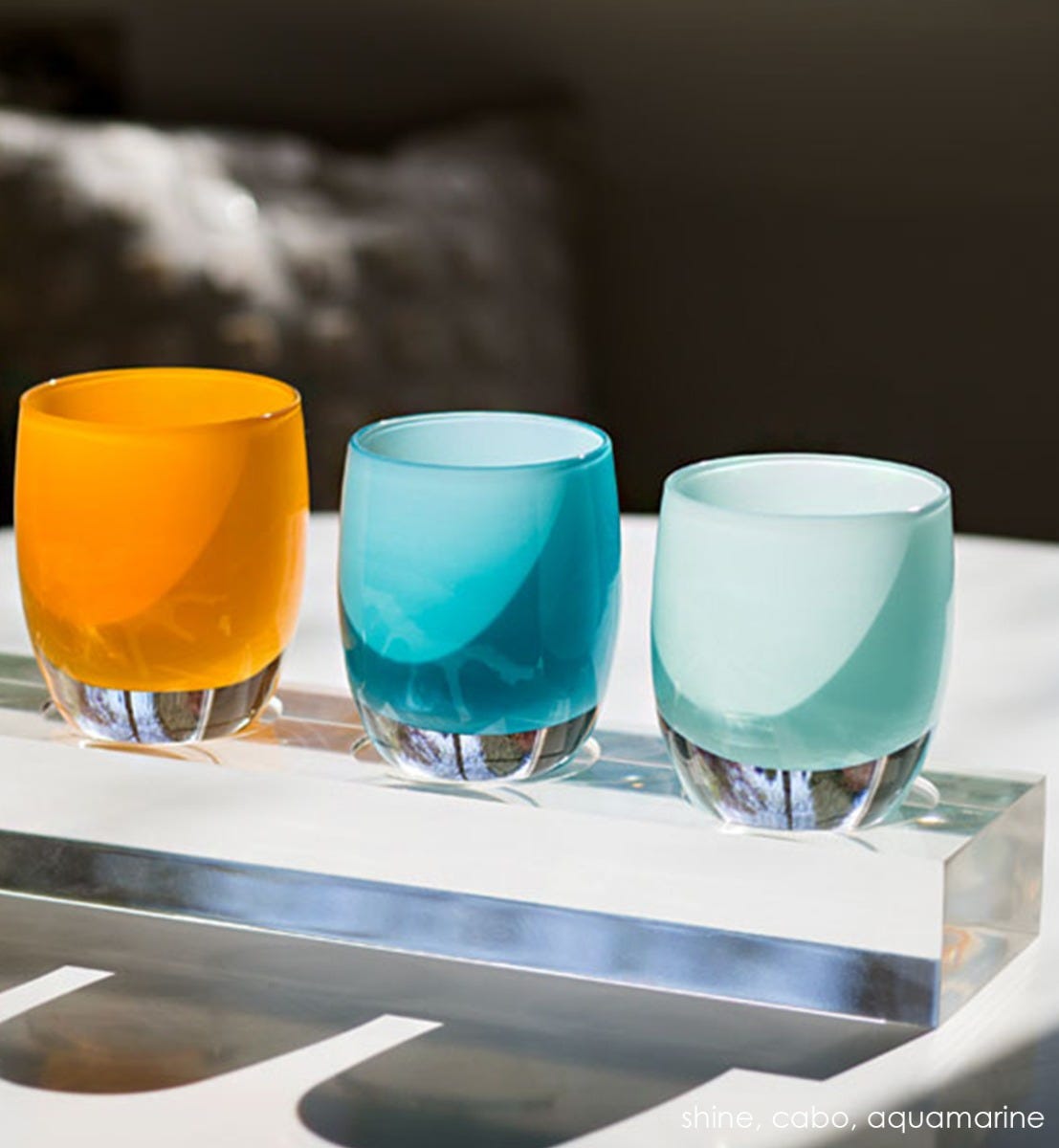 cabo opaque blue hand-blown glass votive candle holder. Paired with aquamarine and sassy on an acrylic stand in the sun.