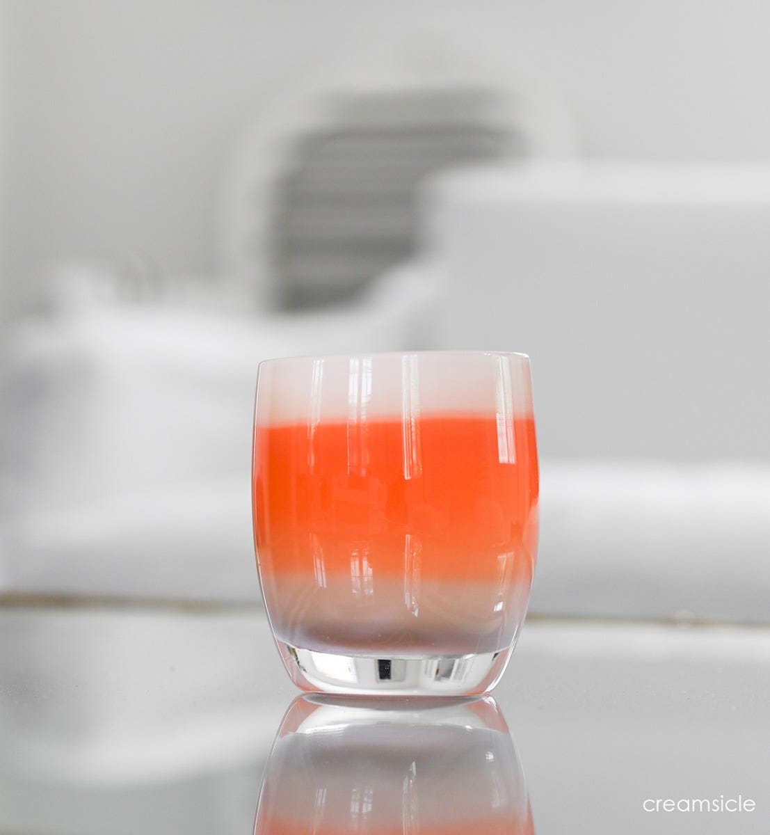 creamsicle orange creamed hand-blown glass votive candle holder sitting on a reflective surface in a white living room.