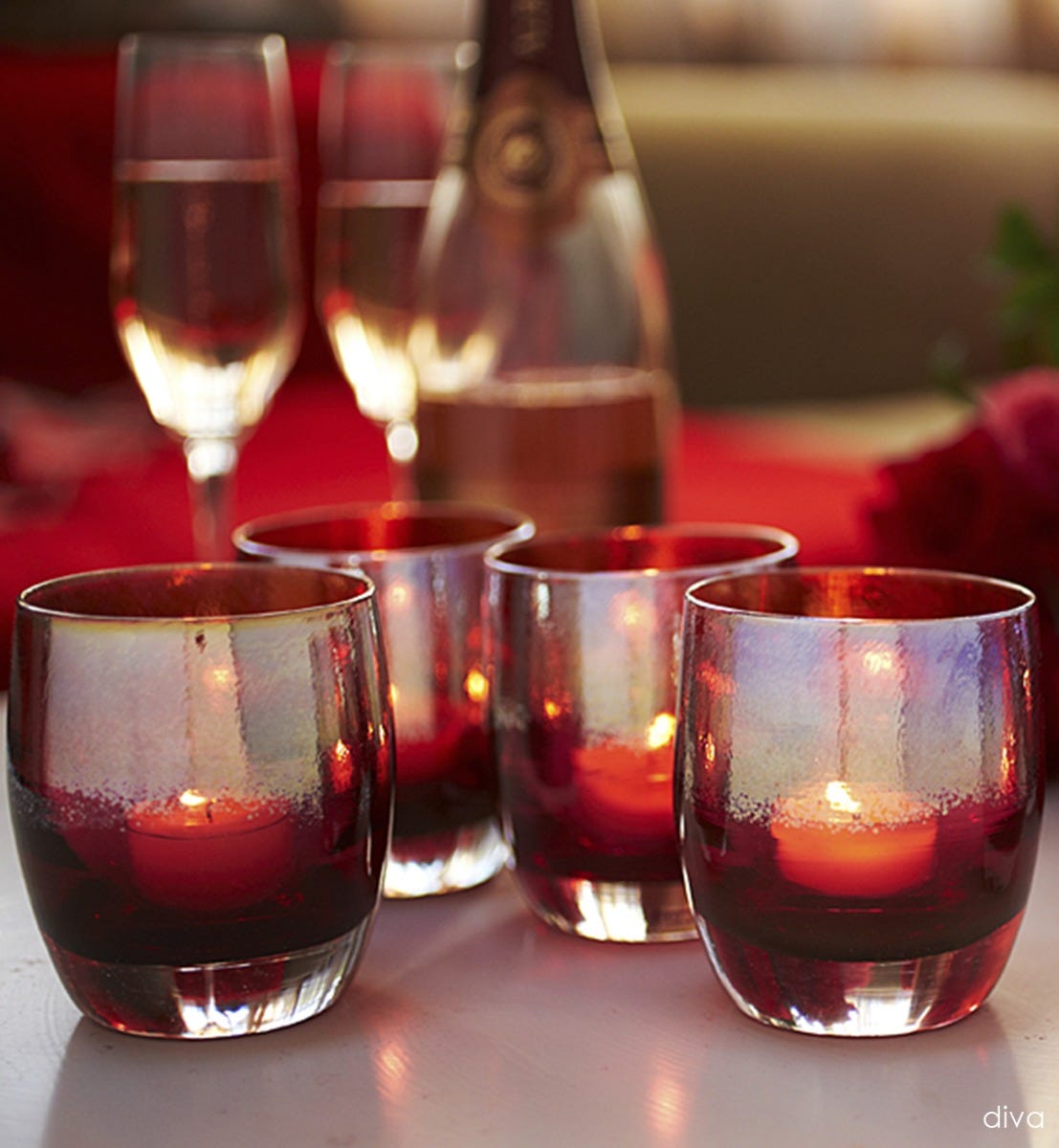 several diva metallic gold on deep pink hand-blown glass votive candle holders with two champagne glasses behind.