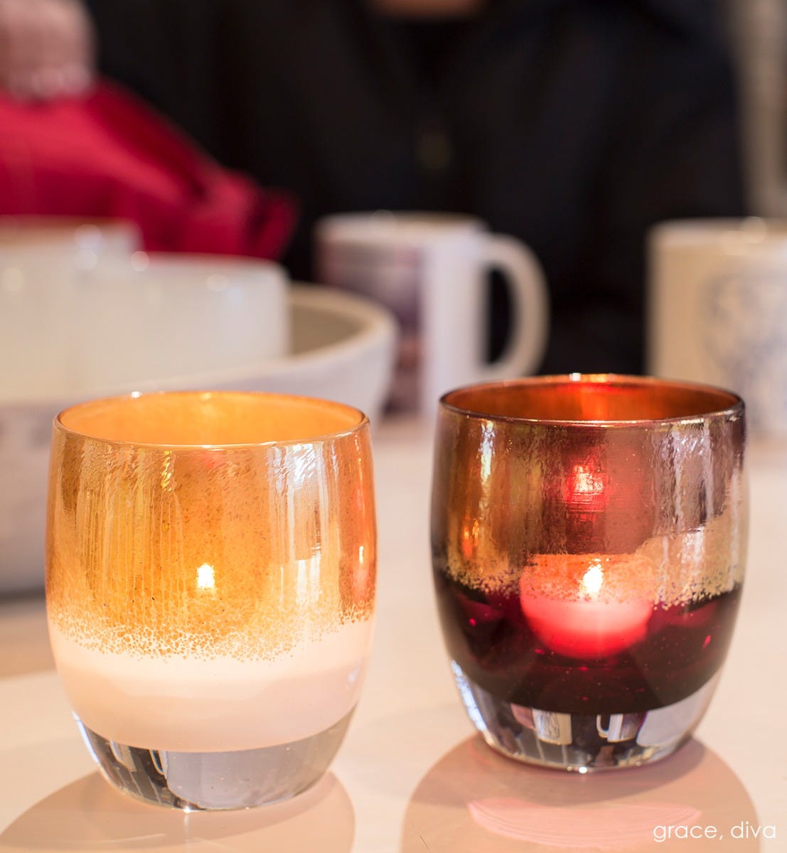 diva metallic gold on deep pink hand-blown glass votive candle holder. Paired with grace on kitchen table with coffee mugs blurred behind.