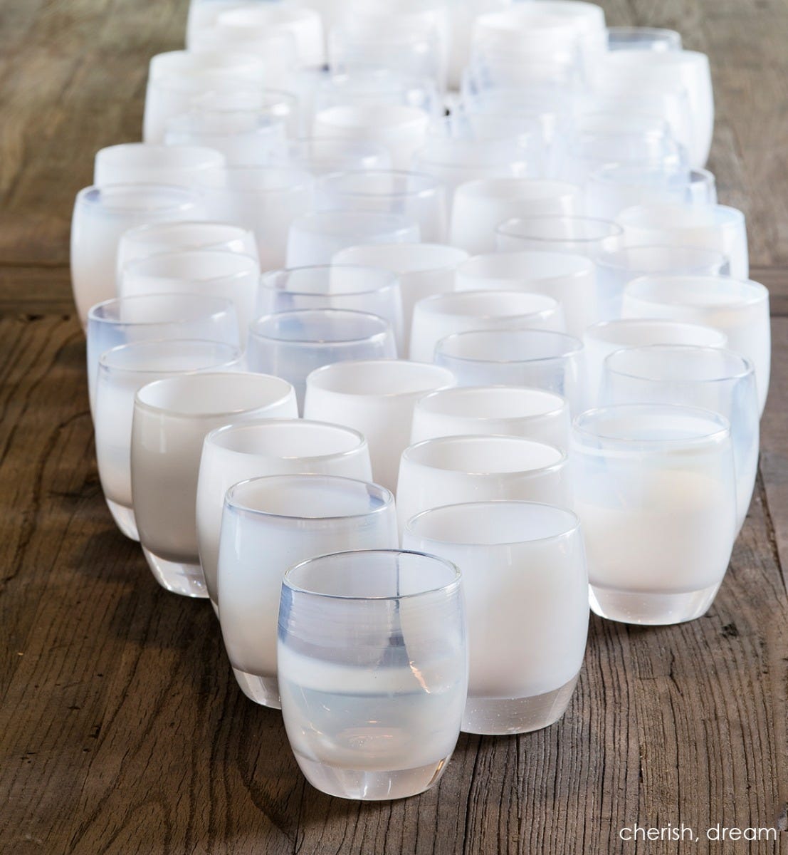 large grouping of dream and cherish. white hand-blown glass votive candle holders on a wood table.