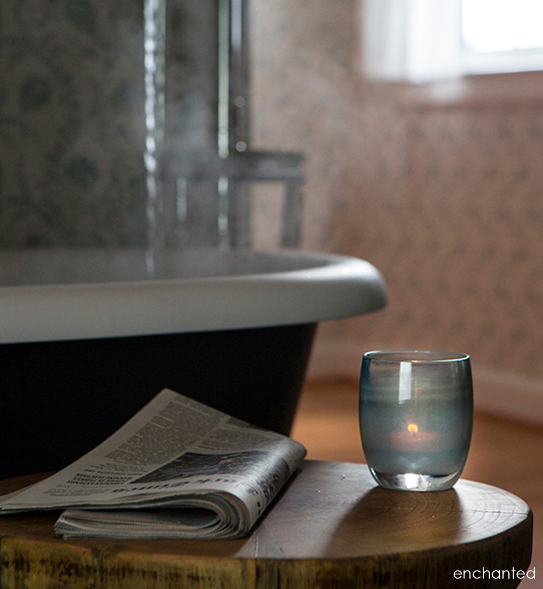 enchanted hand-blown misty green glass votive candle holder. on a tree stump table with a newspaper next to a clawfoot bathtub.