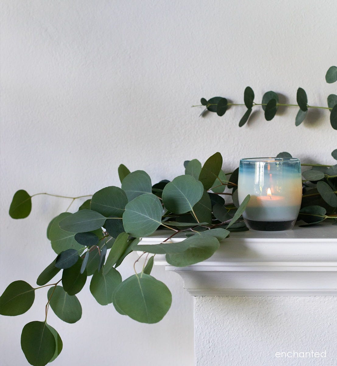 enchanted hand-blown misty green glass votive candle holder on a white fireplace mantle with a decorative green leafy vine.
