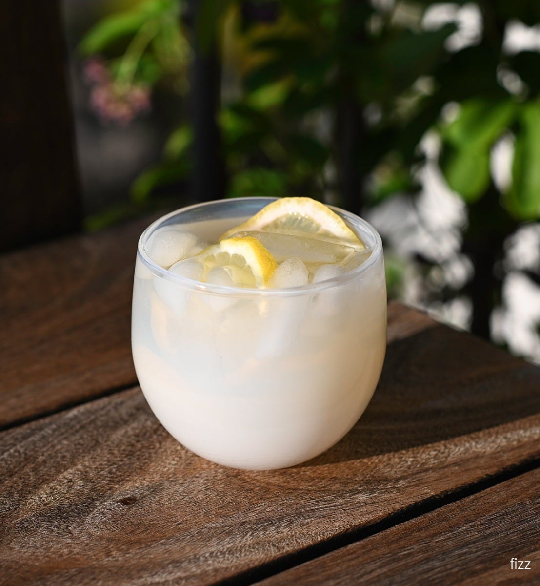 fizz drinker, white hand-blown drinking glass filled with ice, liquid and lemons on a wood table.