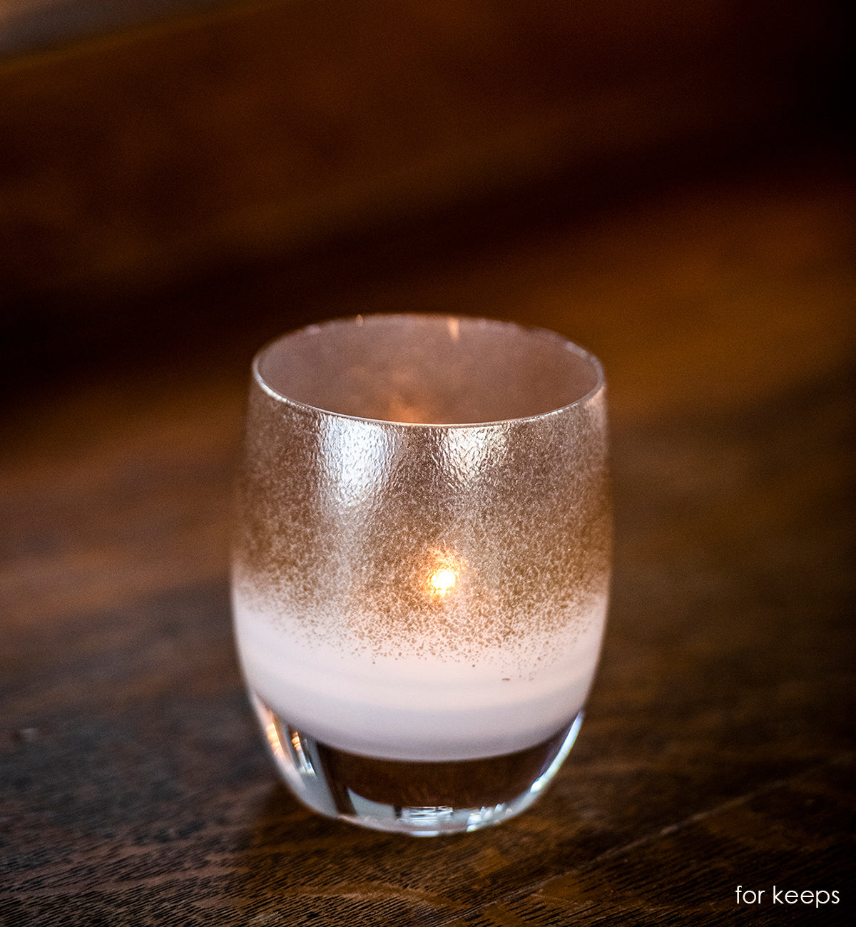 for keeps, beautiful shimmering pewter, hand-blown glass votive candle holder sitting on a dark wood table.