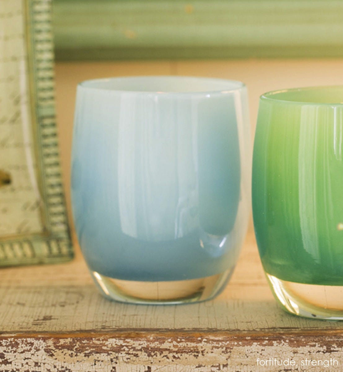 fortitude carolina blue hand-blown glass votive candle holder with strength on a rustic mantle with frame.