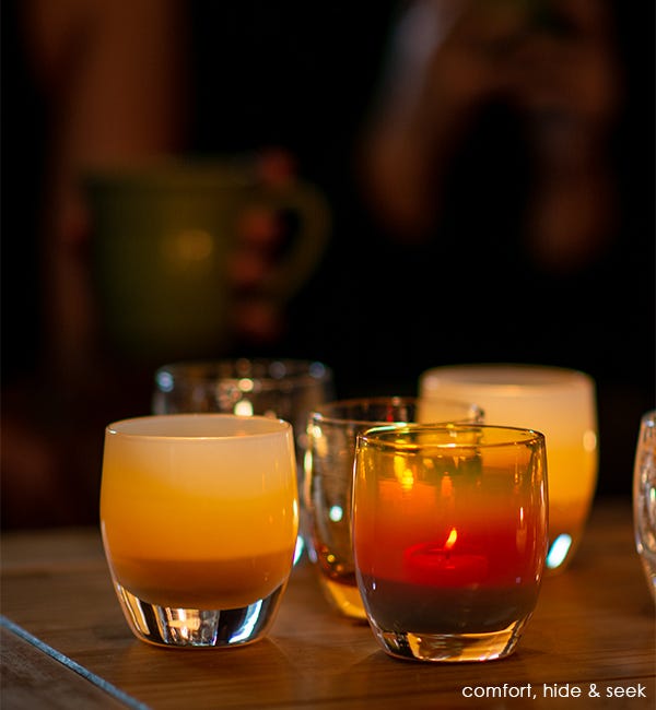 comfort light brown hand-blown glass votive candle holder. Paired with hide and seek on a wood table.