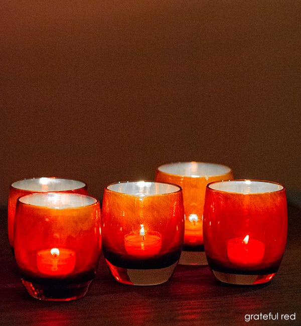 several grateful red wine red with metallic interior hand-blown glass votive candle holders with lit tealights on a dark table in dim lighting.