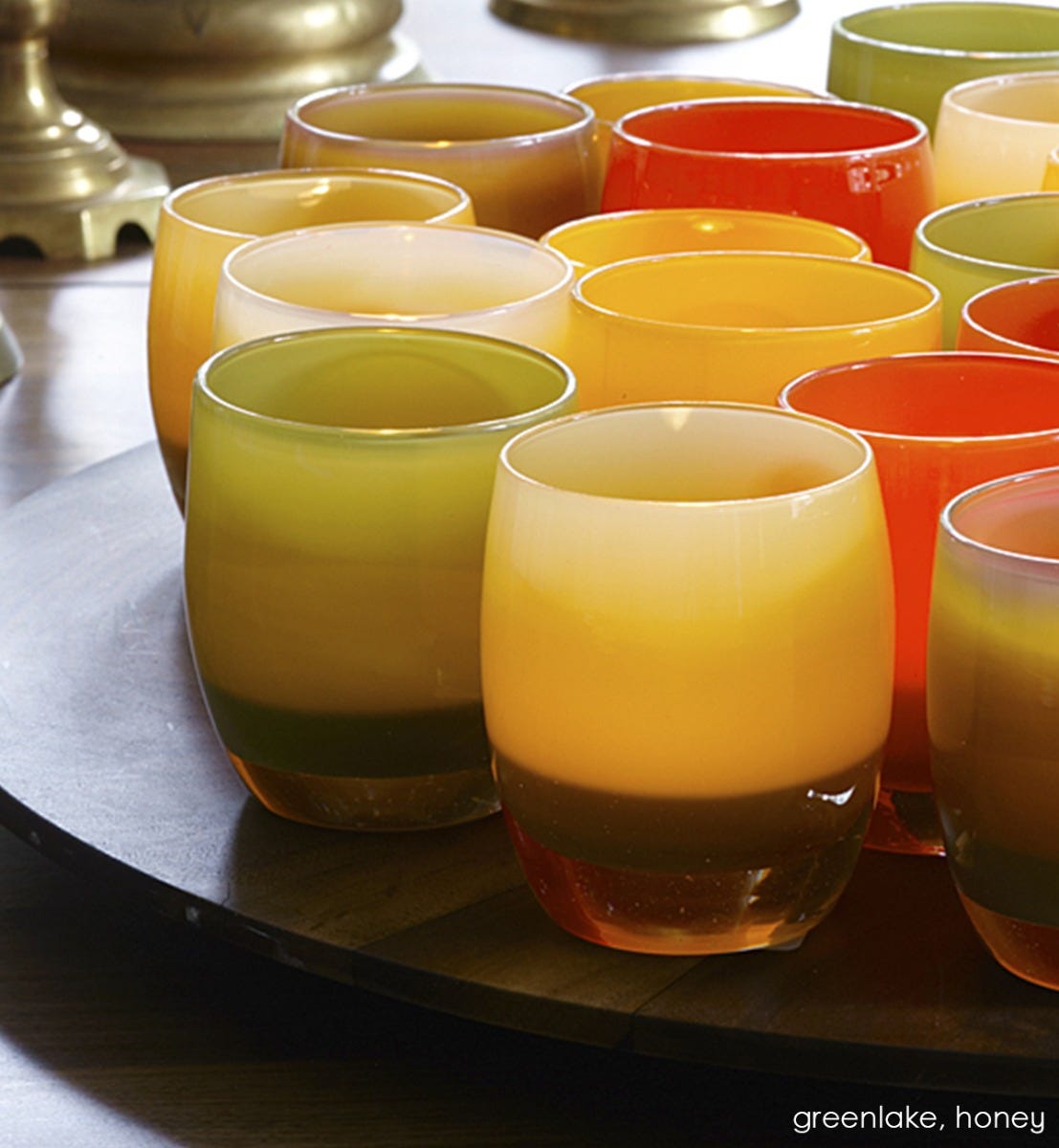greenlake, olive green hand-blown glass votive candle holder with honey and sweet patootie on a round tray on a table.