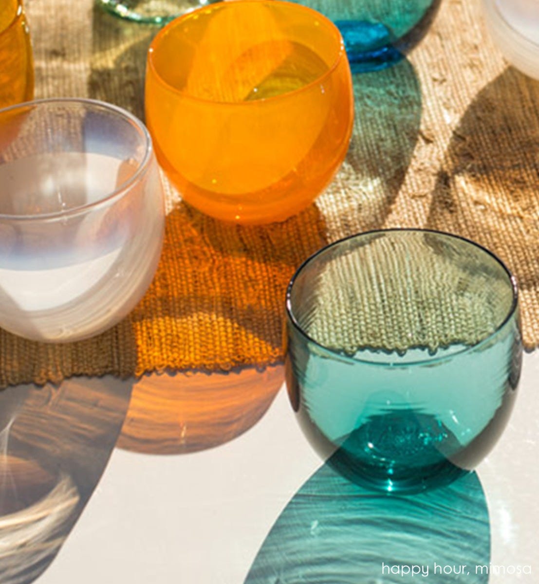 happy hour drinker, natilus blue hand-blown drinking glass sitting on a sunny table with mimosa drinker and fizz drinker with a canvas table runner.