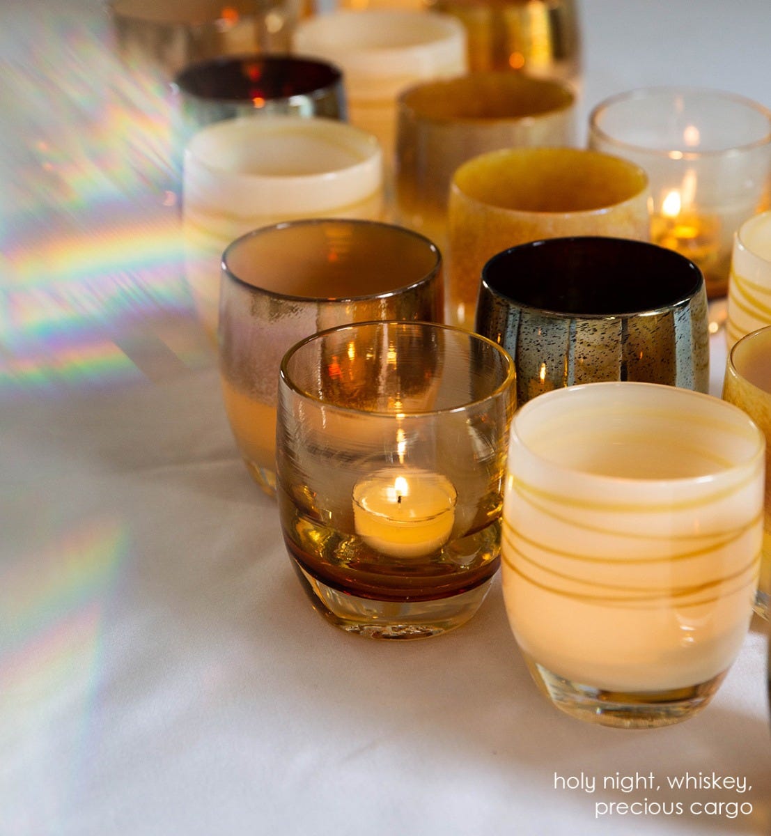 holy night white brown with purple gold metallic wrap, hand-blown glass votive candle holder, with whiskey and precious cargo on a white table clothed table.