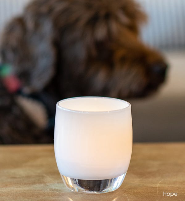 hope pure white hand-blown glass votive candle holder on a light coffee table with brown dog in the background.