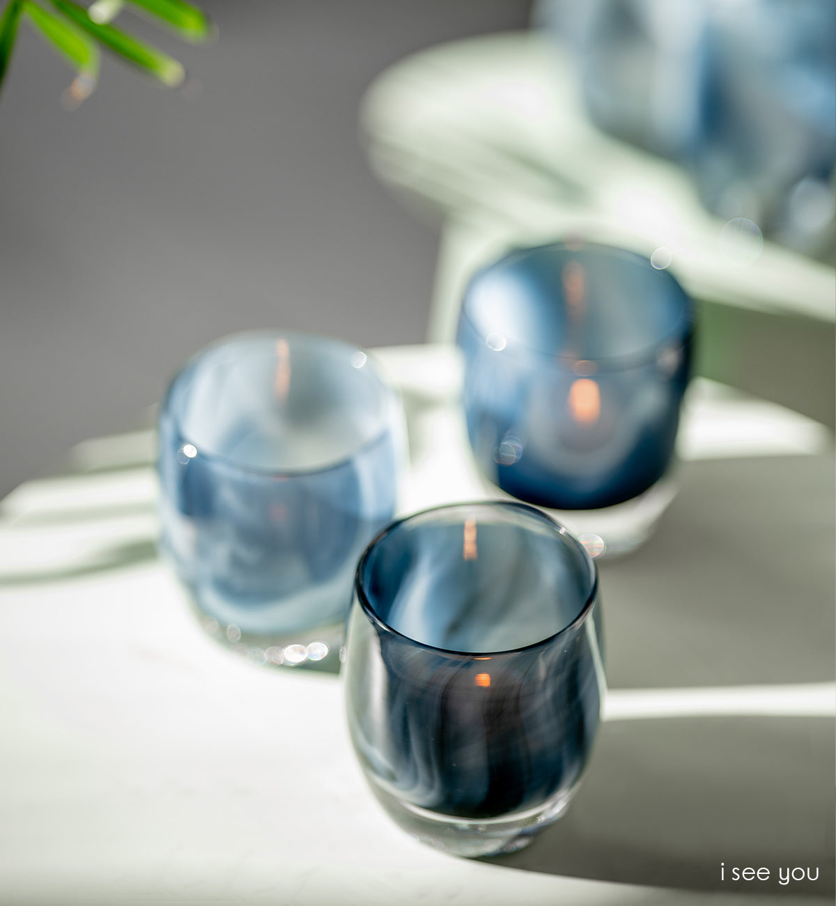 three i see you, smokey blue pattern, hand-blown glass votive candle holders in sunlight on a white living room table.