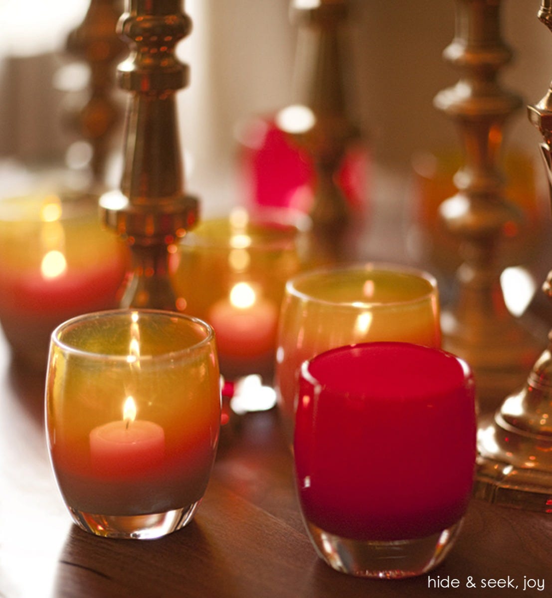 joy crimson red hand-blown glass votive candle holder. Paired with hide and seek on a wood table.