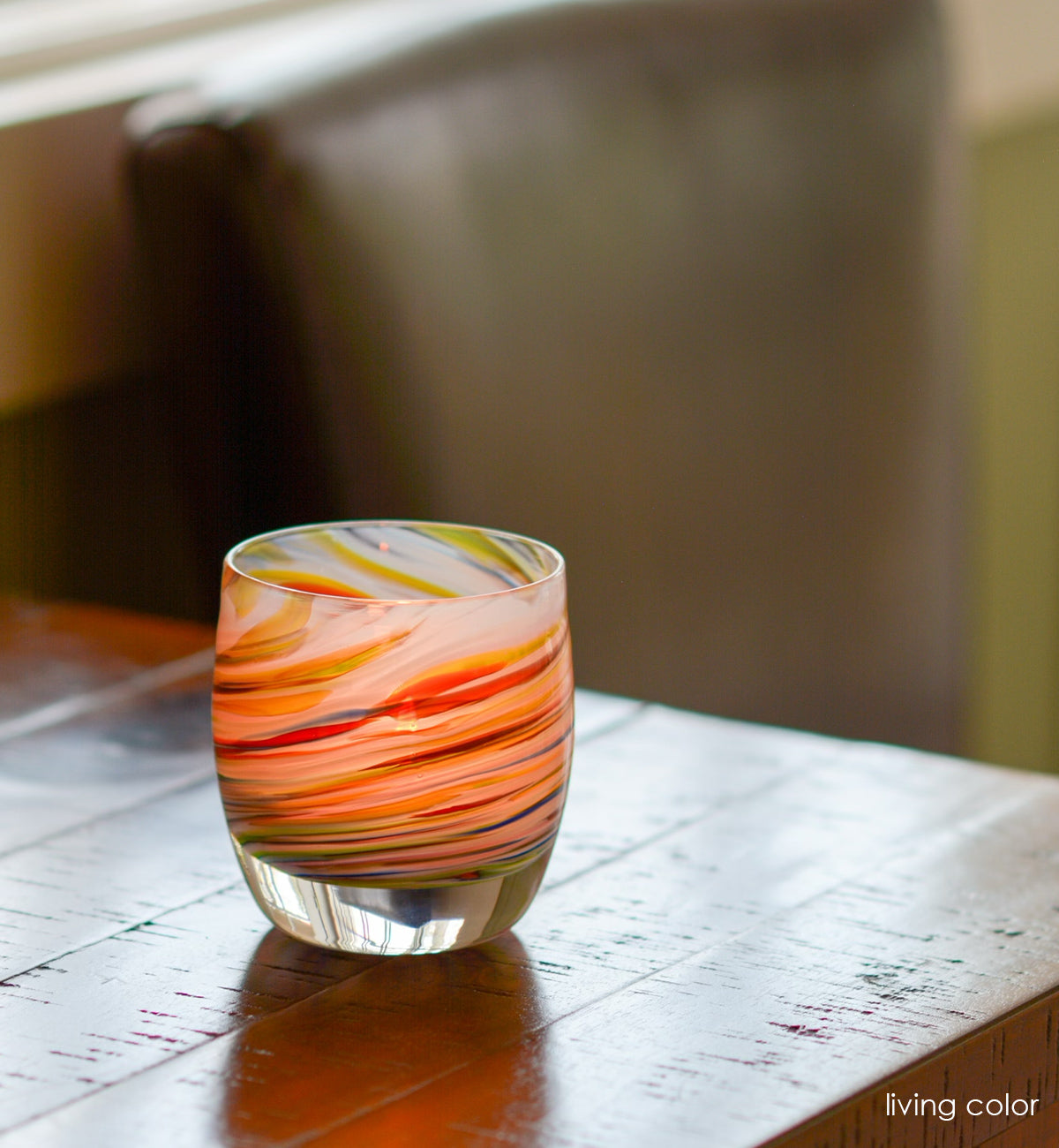 living color hand-blown multicolored swirl, hand-blown glass votive candle holder on a wood table.