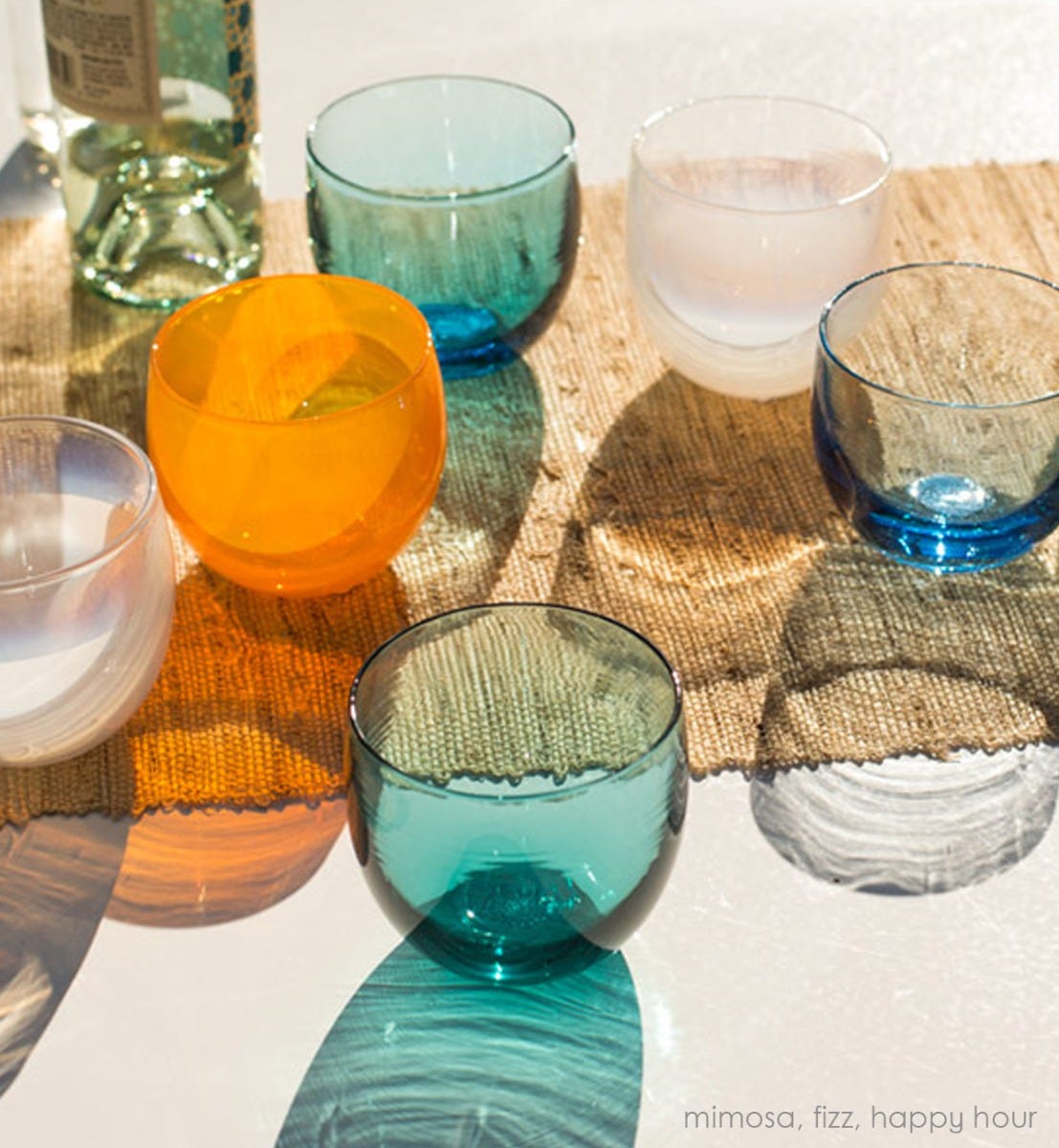 hand-blown tangerine drinking glass in a grouping of fizz drinkers and happy hour drinkers on a sunny outdoor table with a canvas table runner.
