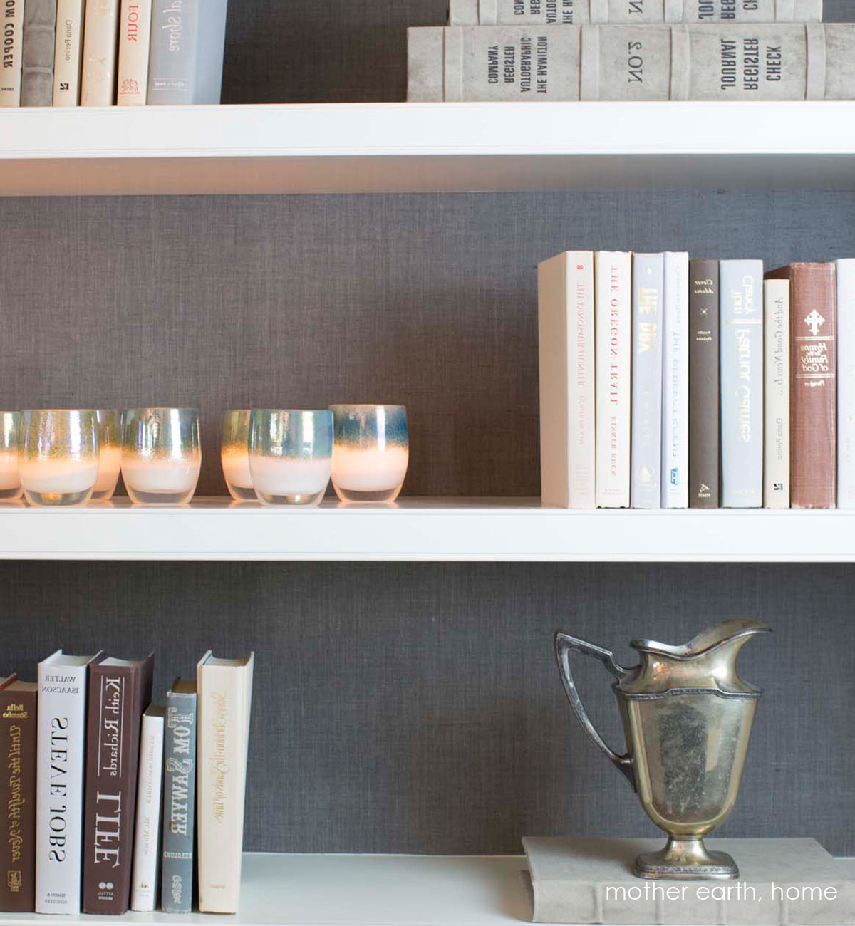 several mother earth white with metallic green blue top, hand-blown glass votive candle holders on a bookshelf.